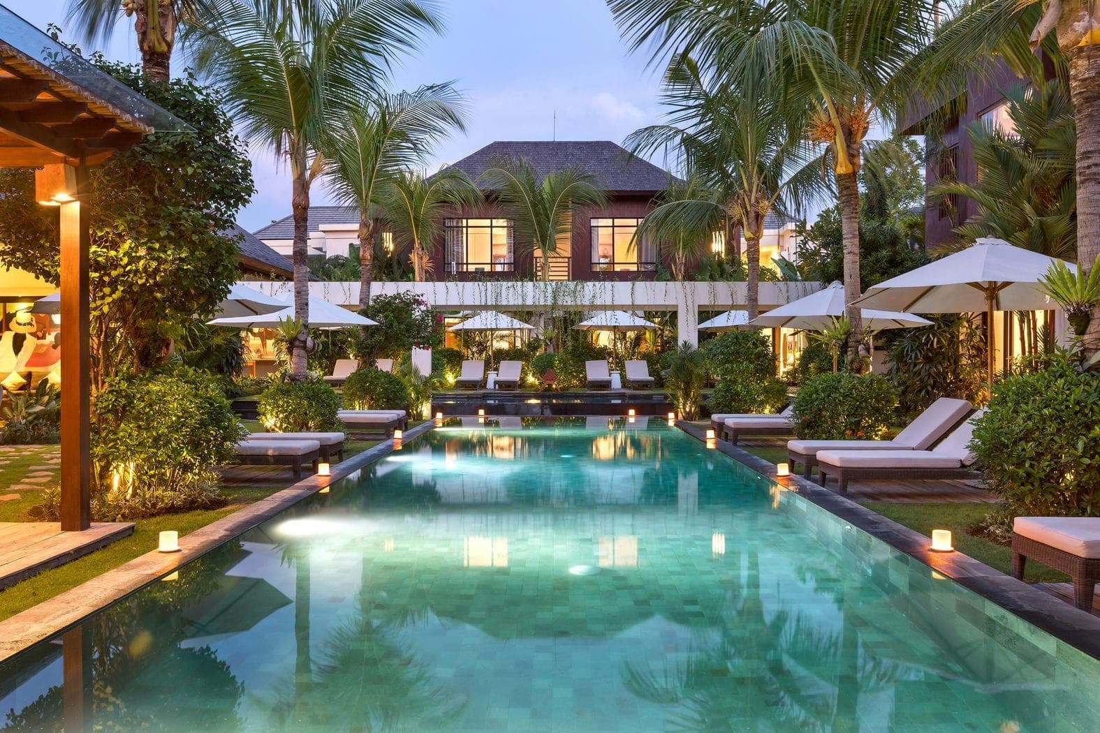 The mirror pool at dusk, sun loungers and candlelight tracing its edge beneath the palms